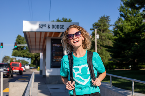 Smiling woman with blue Methodist Health System shirt and sunglasses at a bus stop.